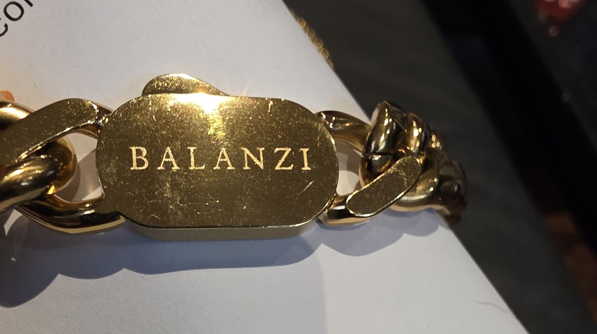 Close-up of a gold BALANZI box clasp showing fine surface scratching across the face